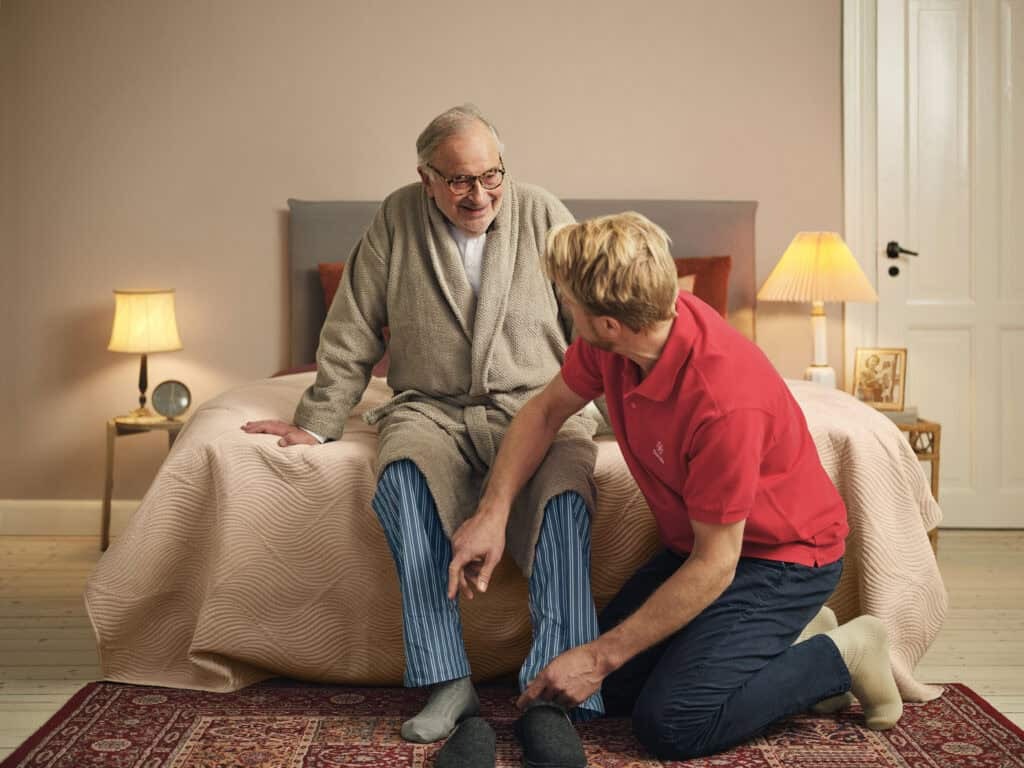 Dovida Caregiver supporting elderly man with getting dressed in a calm home setting